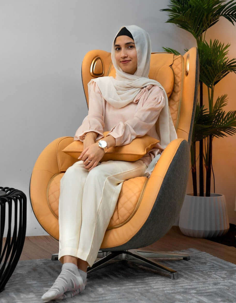 Woman sitting in a modern chair in a stylish room with plants and decor.