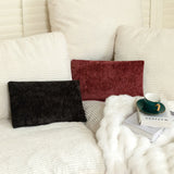 Black and maroon decorative pillows on a cozy sofa with a soft blanket and a green teacup.