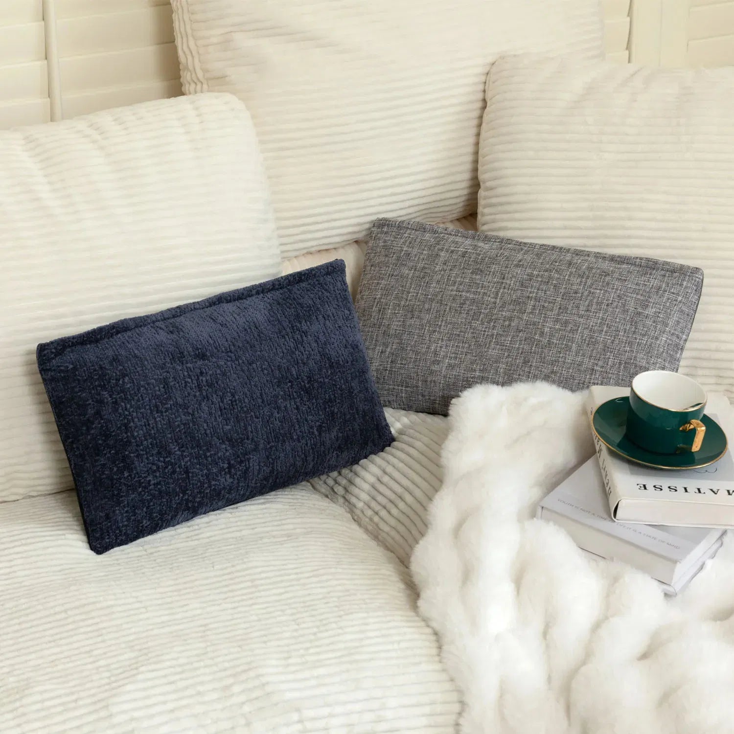 Two stylish pillows in navy and gray on a cozy sofa, surrounded by a soft white blanket and a green coffee cup.